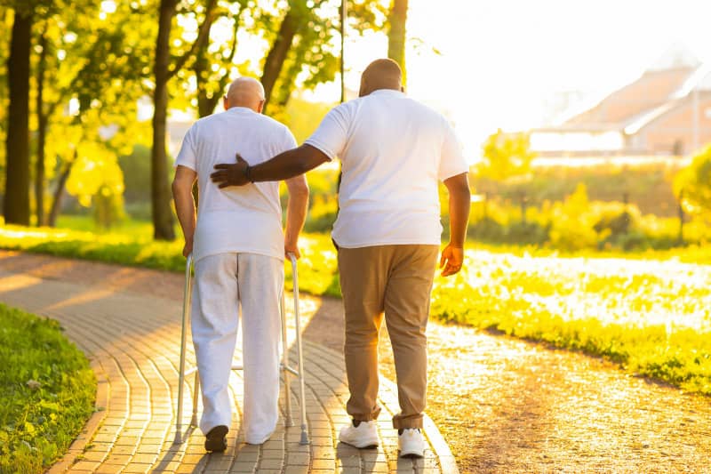 carer with elderly man walking in the garden guiding and caring 
