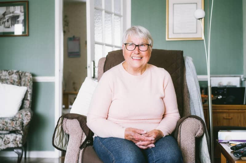 Elderly lady sitting her her chair in her house happy smiling at home  in cirencester uk receiving care from dignity carers 